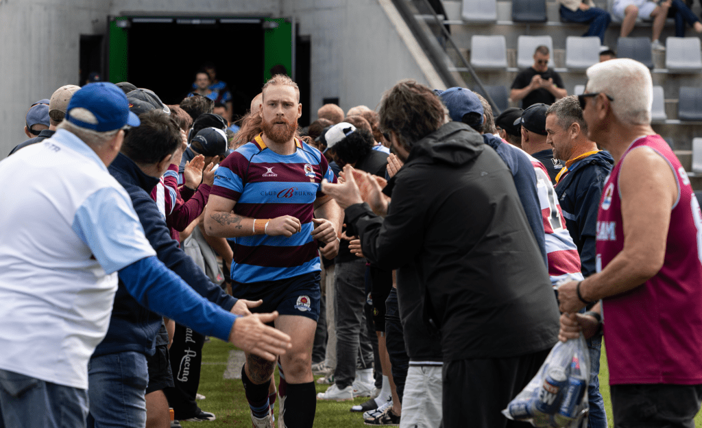 A rugby player runs through a tunnel of cheering fans and teammates before a match, showcasing team spirit and enthusiasm in a sports setting.