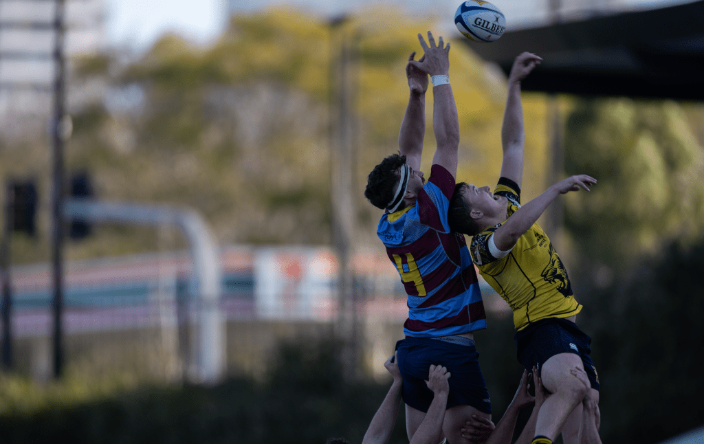 Two rugby players jumping to catch a ball during a match.