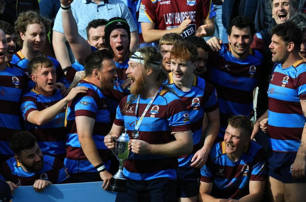 A group of ecstatic rugby players celebrating a victory, with one player holding a trophy at the forefront.